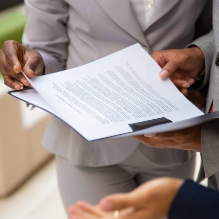 Diverse business partners reading contract together. Business man and woman wearing formal suits, standing and holding open folder with document. Agreement concept